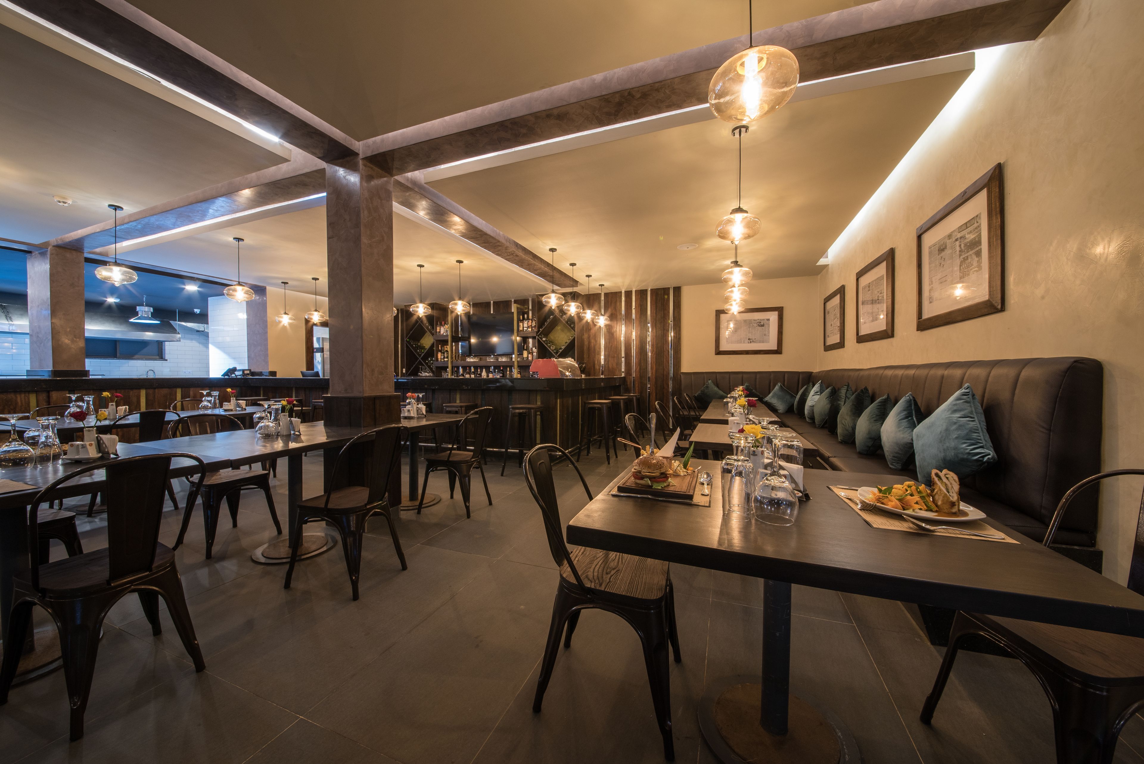 Um restaurante moderno com mesas comunitárias compridas, cadeiras de madeira escura e um bar ao fundo.
