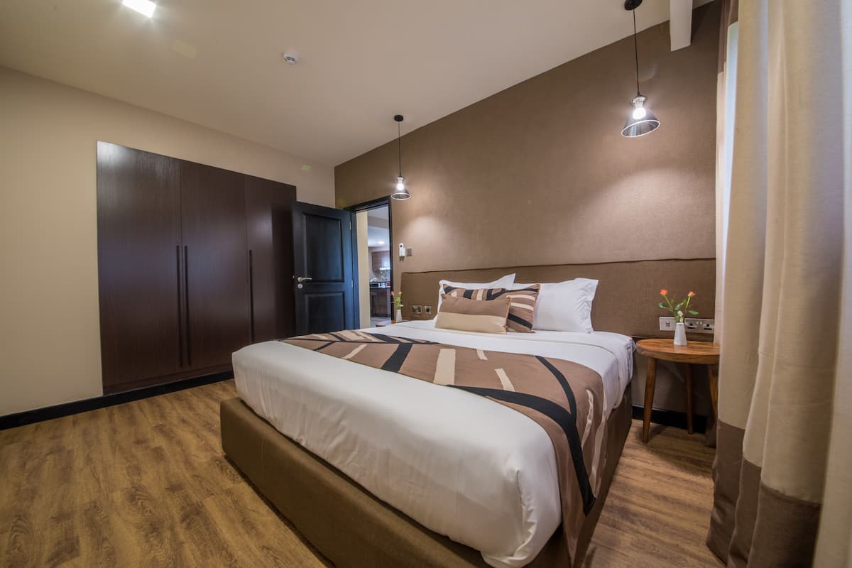 A hotel room with a large bed, a wardrobe, a bedside table with a vase, and a hanging light fixture.