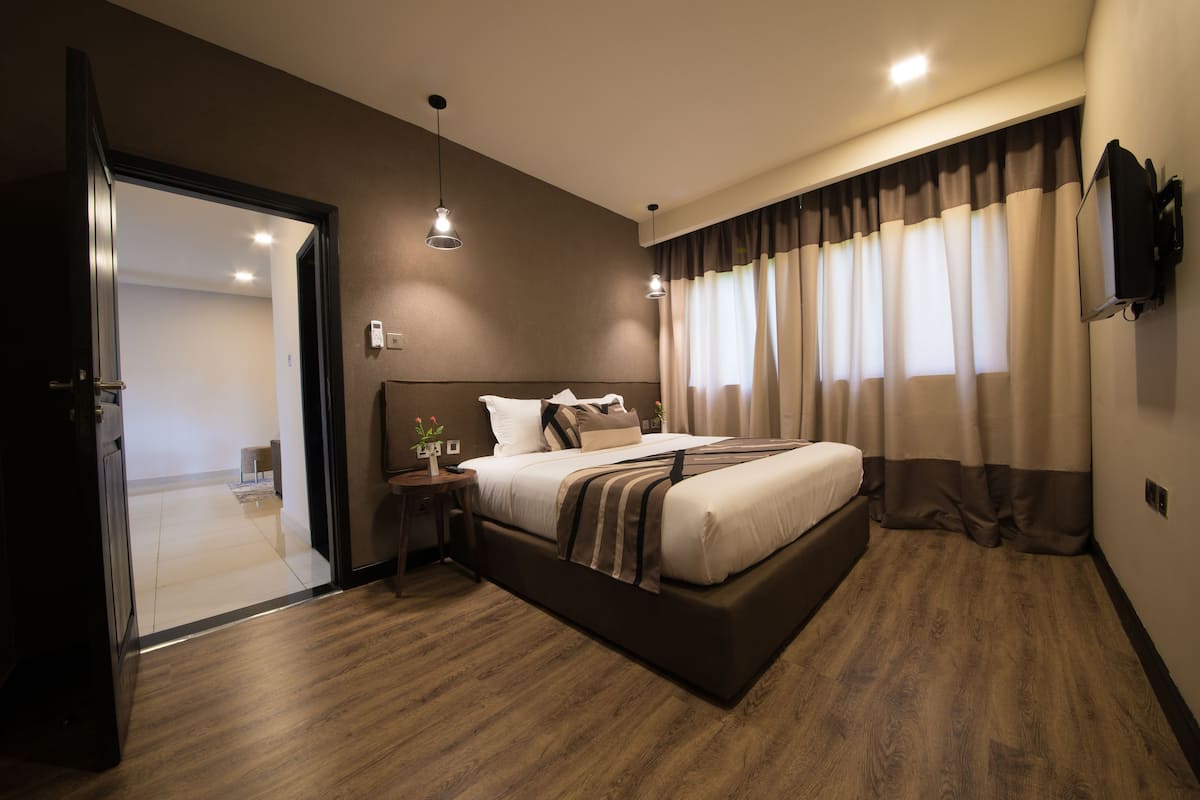 A modern bedroom with a large bed, bedside tables, a TV, and a view of a hallway.