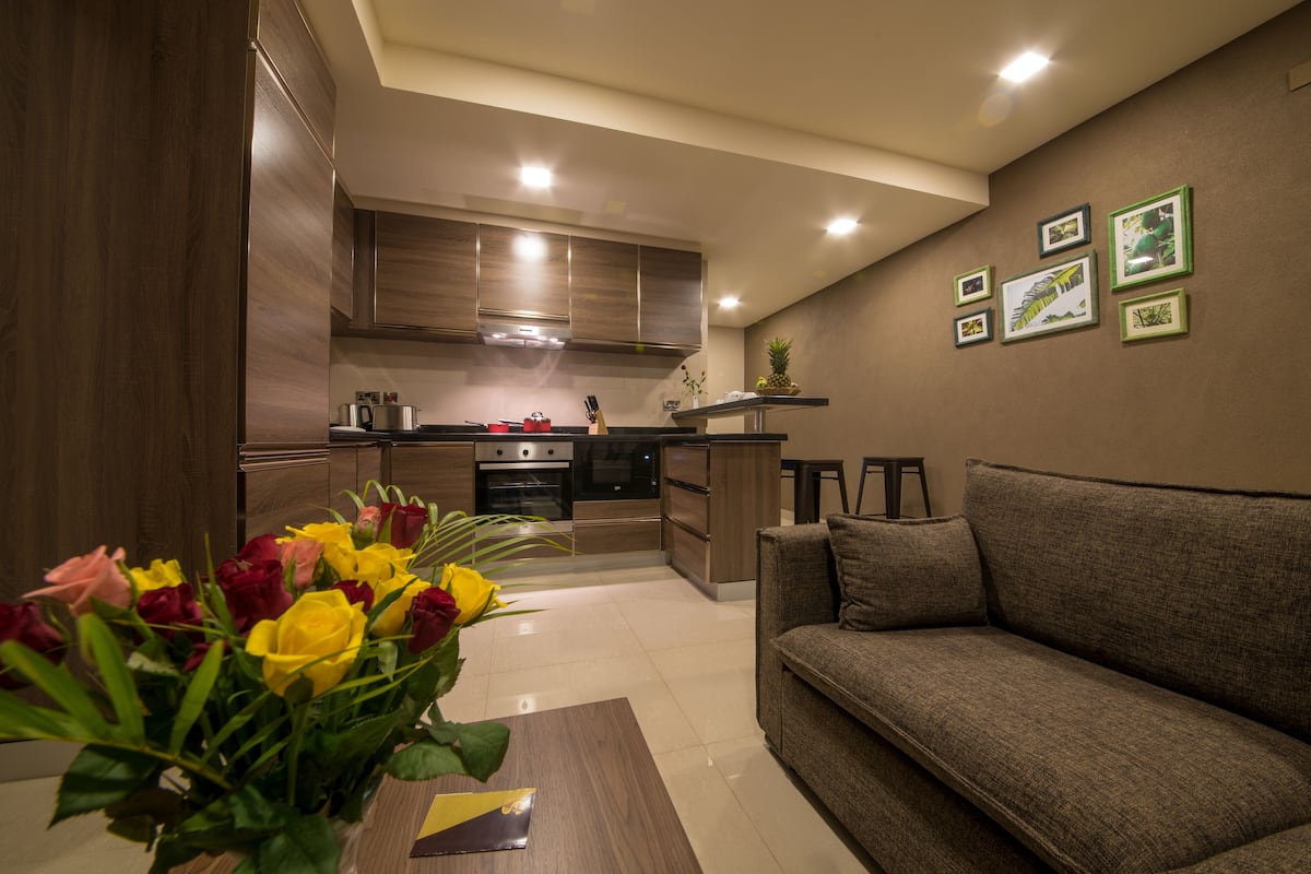 A modern kitchen with wooden cabinets, a built-in oven, and a dining area with a brown sofa and a coffee table.