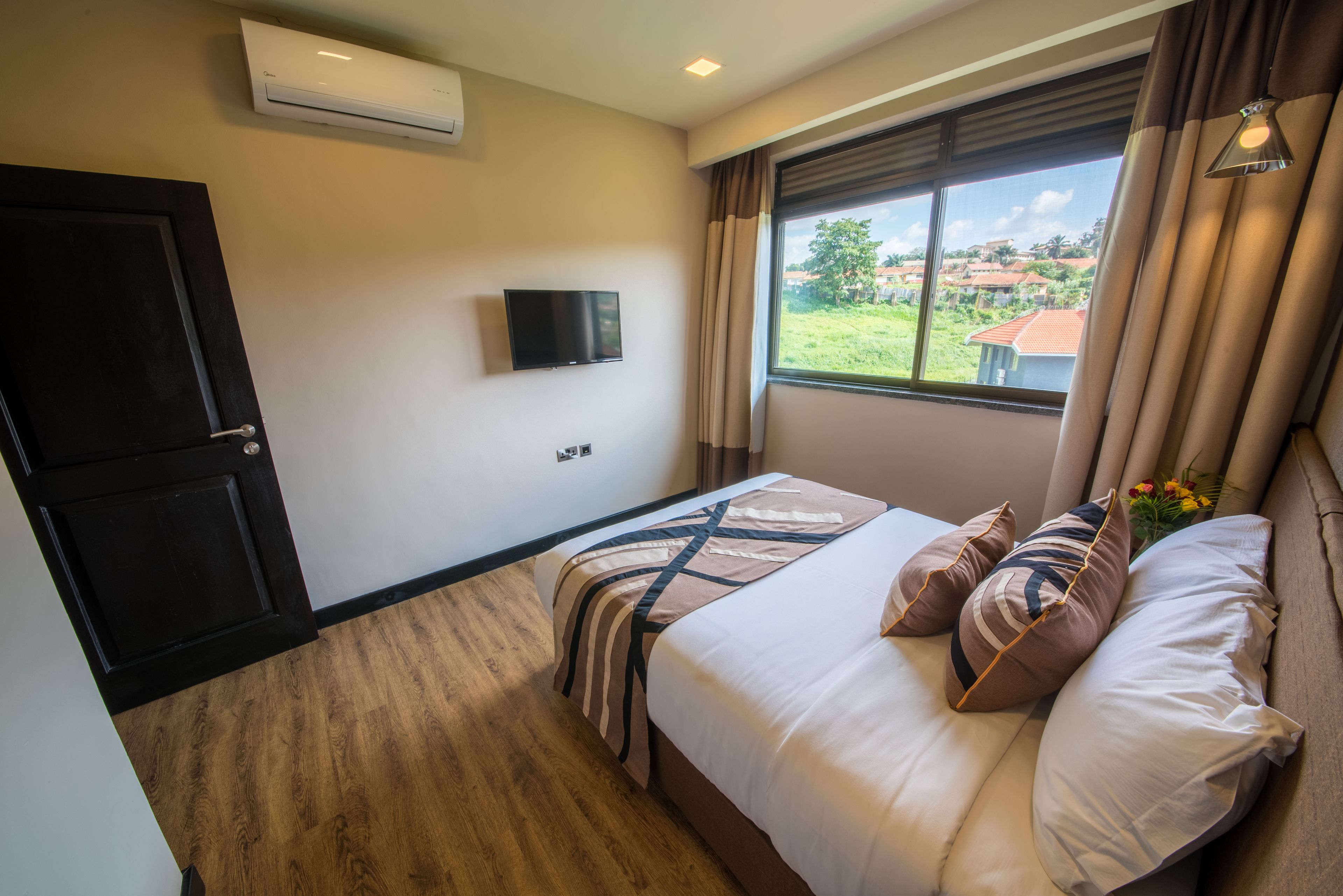 A hotel room with a bed, a TV, an air conditioner, and a window with a view of the outside.