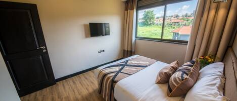 Habitación de hotel con cama, televisión, aire acondicionado y ventana con vistas al exterior.