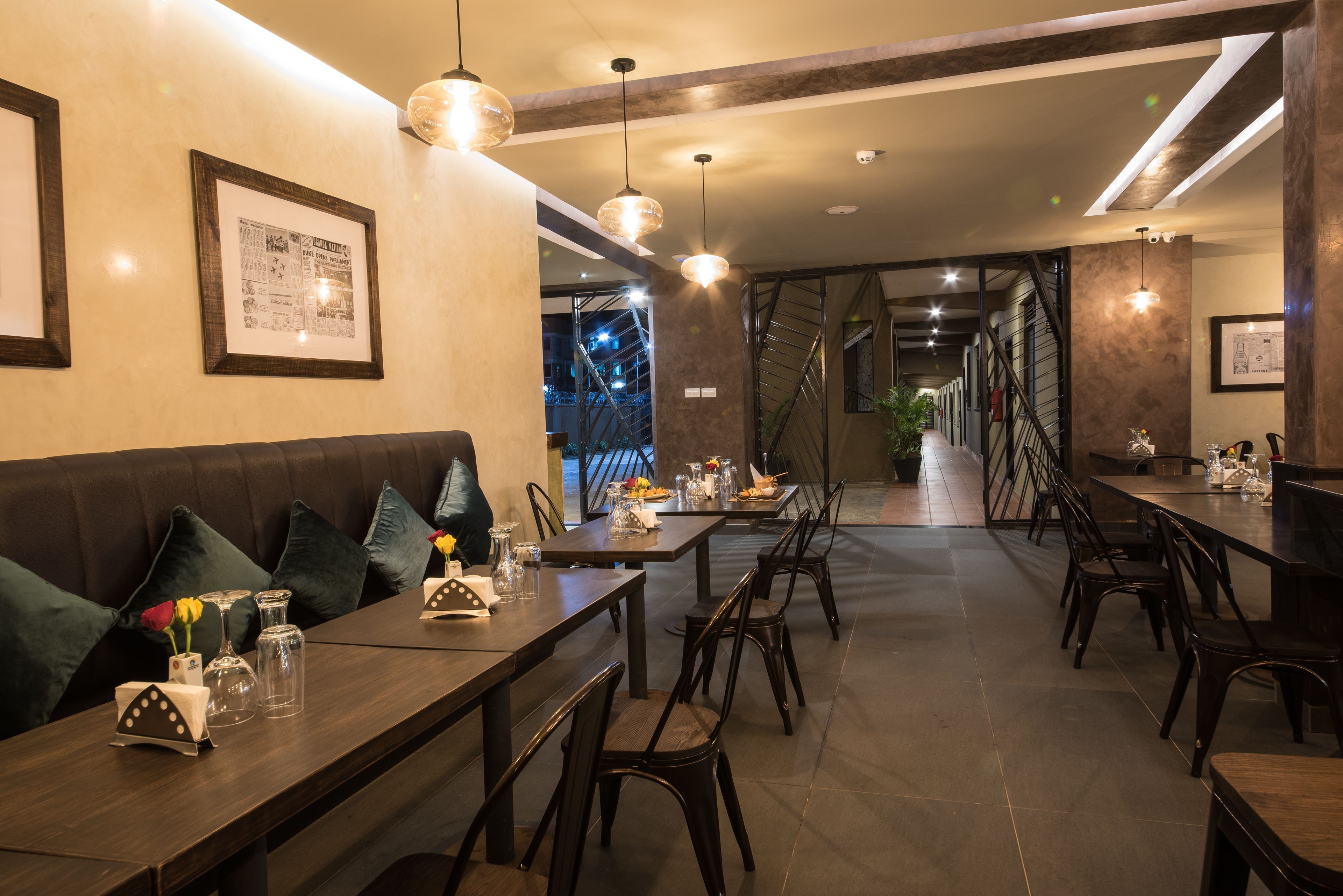 A restaurant with wooden tables and chairs, pendant lighting, framed pictures on the walls, and a staircase leading to an upper level.