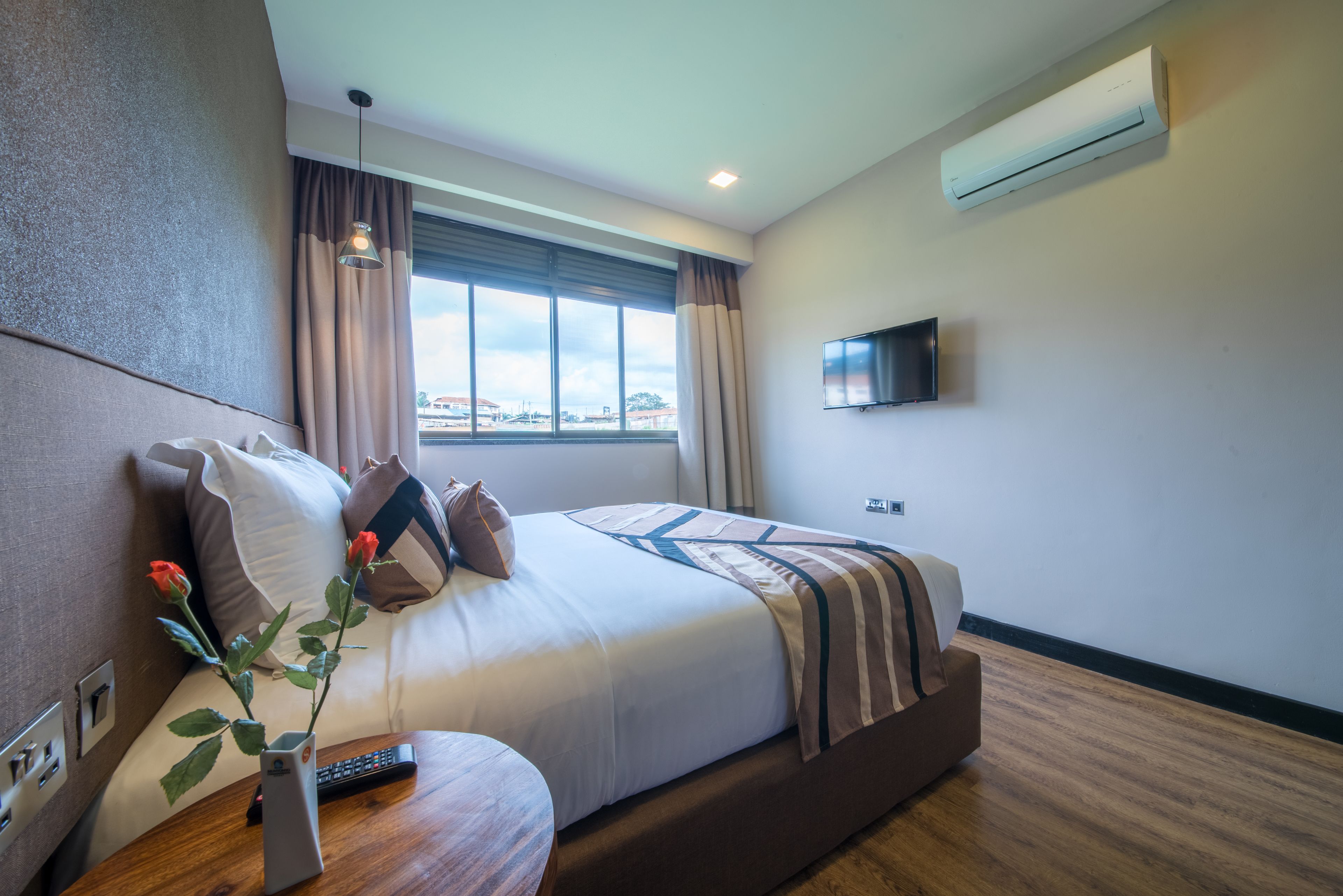 Una habitación de hotel moderna con una cama grande, un televisor montado en la pared y una ventana con cortinas.