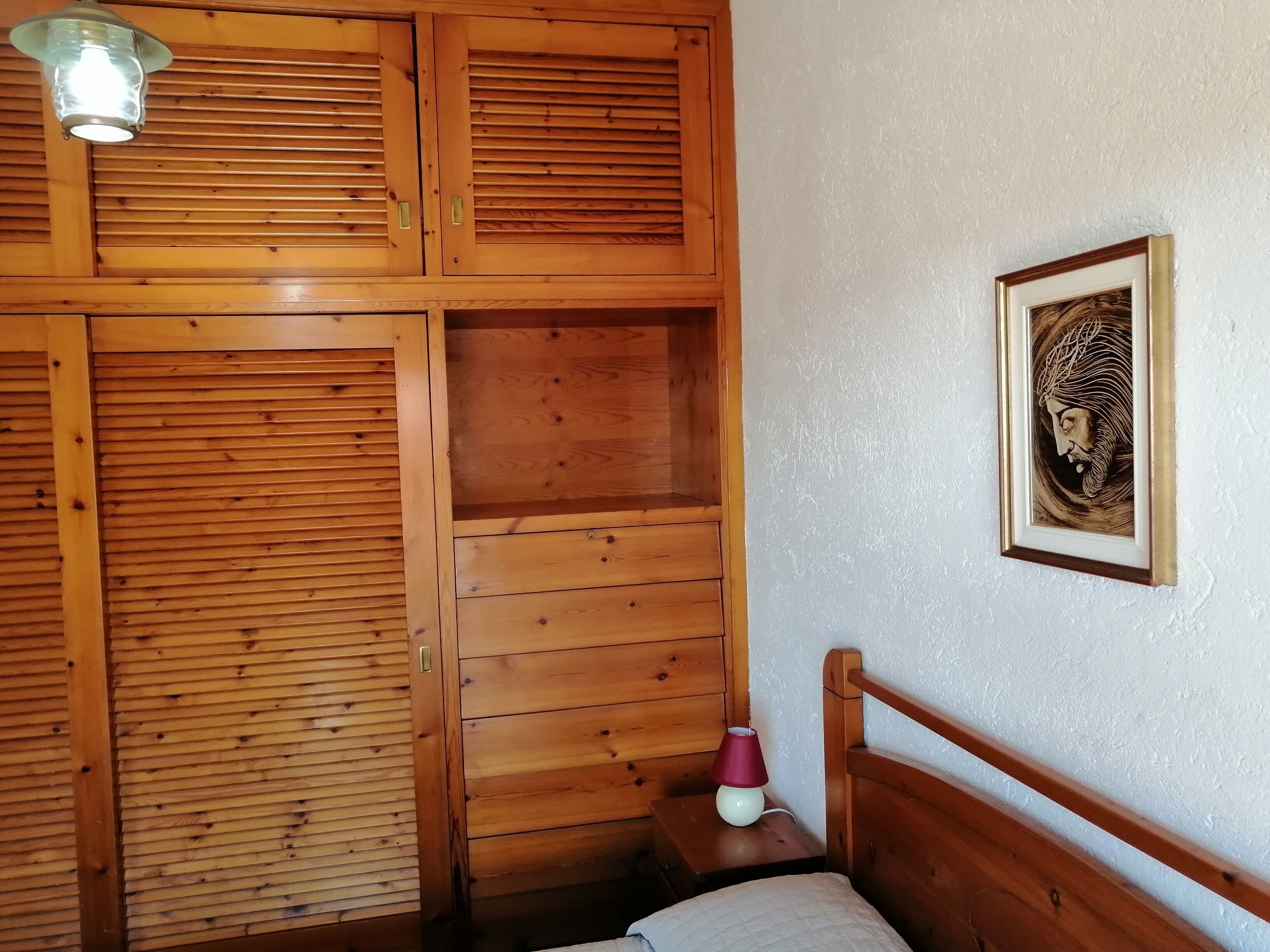A wooden room with a bed, a nightstand, a lamp, and a framed picture on the wall.