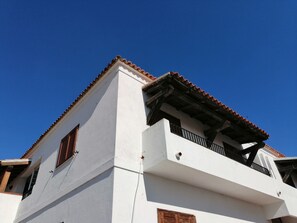 A white building with a red-tiled roof, wooden balconies, and a clear blue sky. - Aria di Vacanza- Molara (Loiri Porto San Paolo)