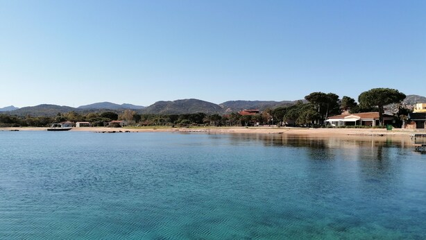 A clear lake with a boat, surrounded by buildings and trees. - Aria di Vacanza- Molara (Loiri Porto San Paolo)