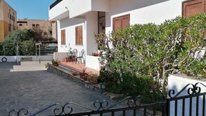 A white building with a balcony, stone-paved courtyard, and potted plants. - Aria di Vacanza- Molara (Loiri Porto San Paolo)