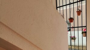 A staircase with a white wall and a window with black bars. There are potted plants on the windowsill and a small garden area with pebbles and plants at the base of the stairs. - Aria di Vacanza- Molara (Loiri Porto San Paolo)