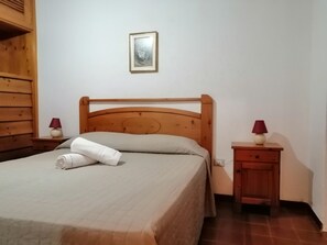 A neatly made bed with a wooden headboard, a small bedside table with a lamp, and a wall-mounted picture. - Aria di Vacanza- Molara (Loiri Porto San Paolo)
