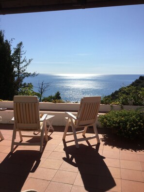 Two white lounge chairs facing a patio with a view of the sea. - B&B Le Tre Casette (Maratea)