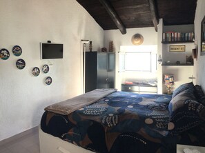 Une chambre à coucher comprenant un lit, une télévision, une armoire, une étagère avec des livres et des assiettes décoratives accrochées au mur.