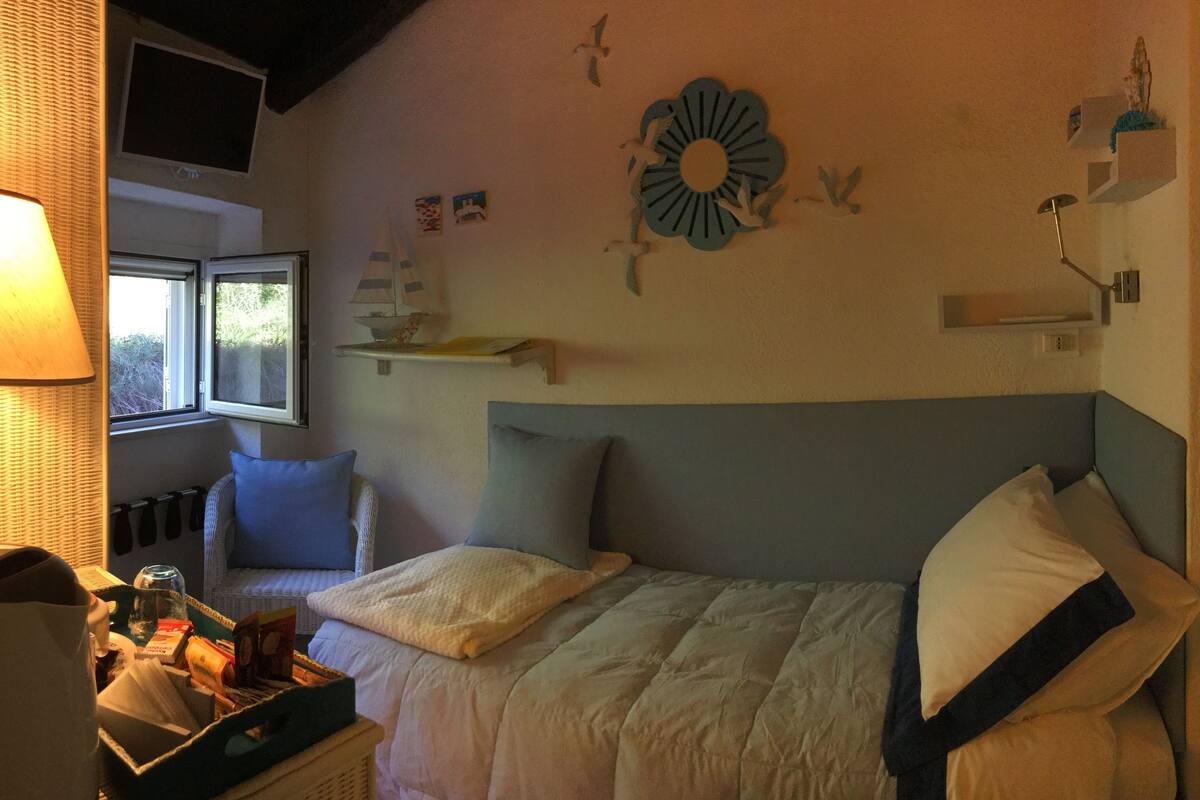 Un dormitorio con cama, una silla, una lámpara, un ventanal y adornos en la pared.