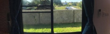 Una habitación con un amplio ventanal que da a un área verde y una pared de concreto.