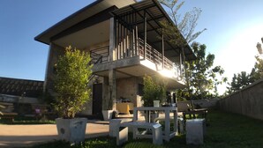 A modern two-story building with a balcony, concrete pillars, and potted plants. - Ban Roojai (Nan)