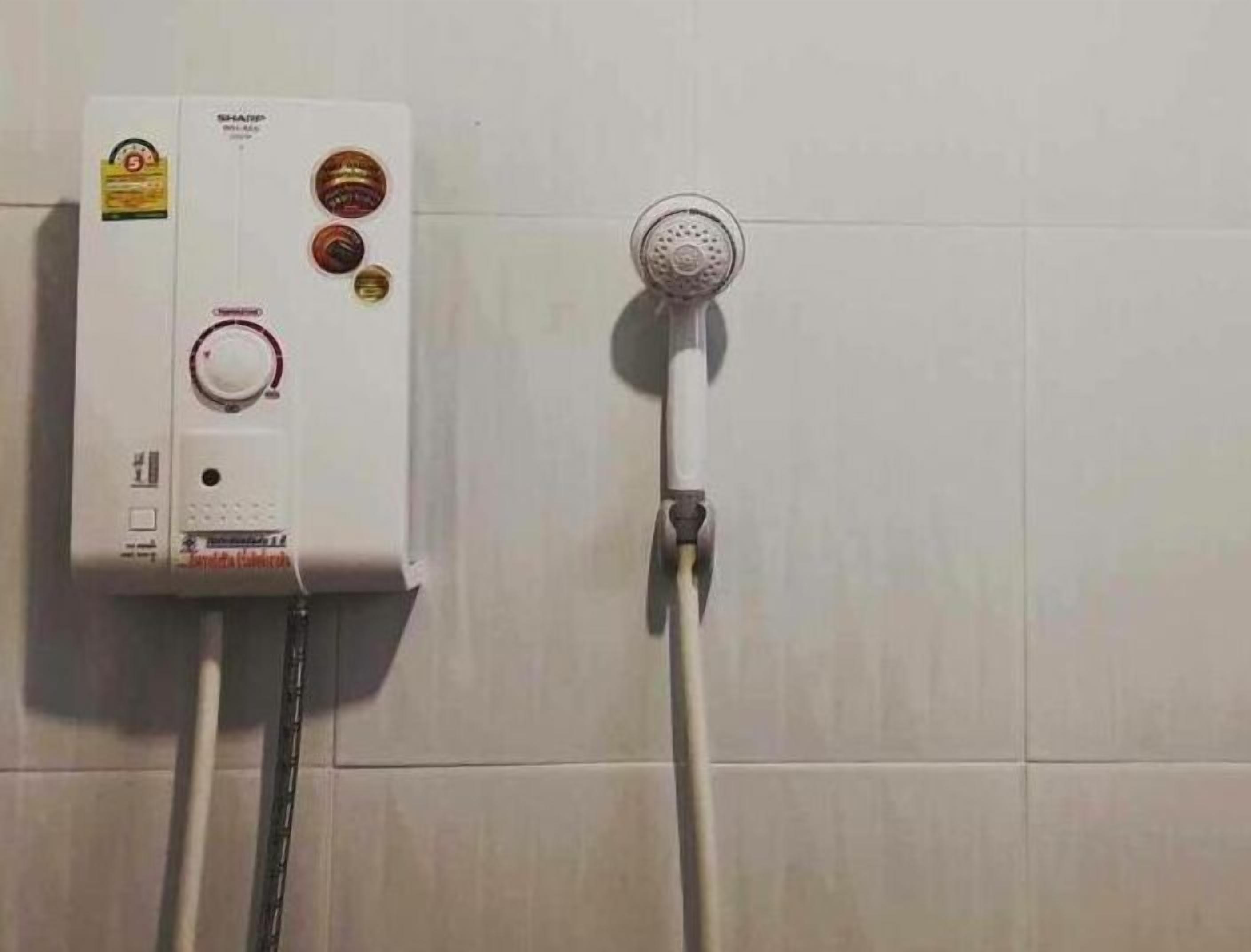 Ein Warmwasserbereiter mit Drehregler und Duschkopf an einer gefliesten Wand.