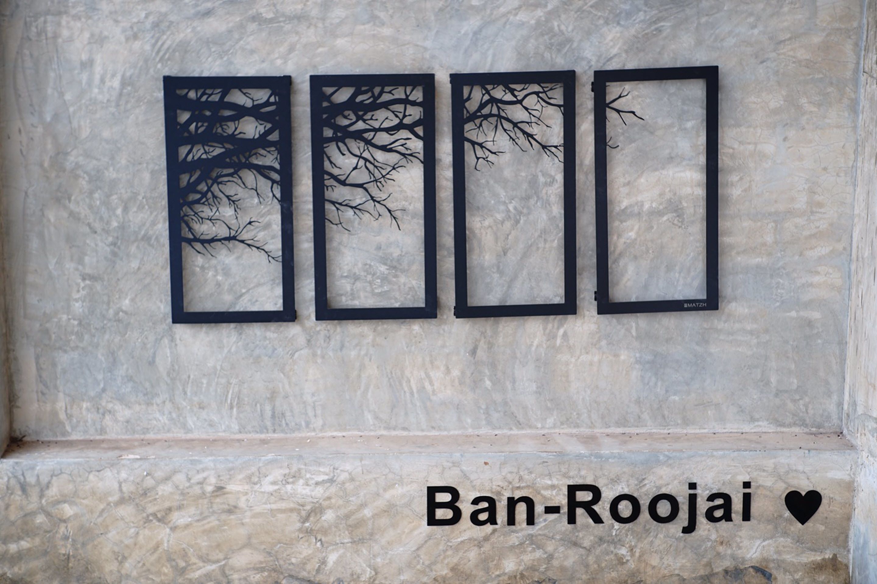 Four black tree silhouettes on a marble wall, with the text "Ban-Roojai" and a heart symbol below.