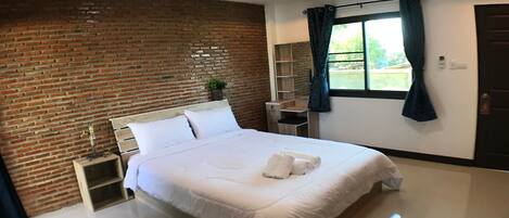 Quarto de hotel moderno com parede de tijolos, uma cama grande com lençóis brancos, uma pequena mesa de cabeceira com abajur e uma janela com cortinas.