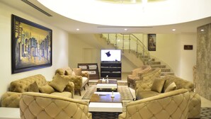 Un salón amplio con un televisor grande, asientos cómodos y una escalera que lleva a un nivel superior.