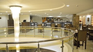 Un restaurante moderno con barandilla de cristal, un candelabro central y una zona de estar con mesas y sillas.