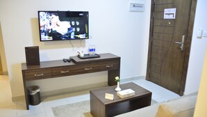 Una sala de estar moderna con un televisor de pantalla plana montado en la pared, una mesa consola de madera con una bandeja, un jarrón pequeño y un cesto de basura.