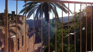 A stone building with a narrow passageway, a large palm tree, and a view of distant hills. - Off The Square (Safed)