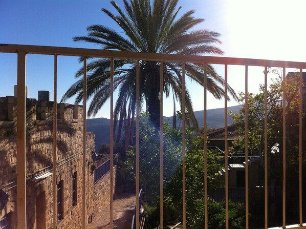 Un edificio de piedra con un estrecho pasaje, una palmera grande y vistas a colinas distantes.