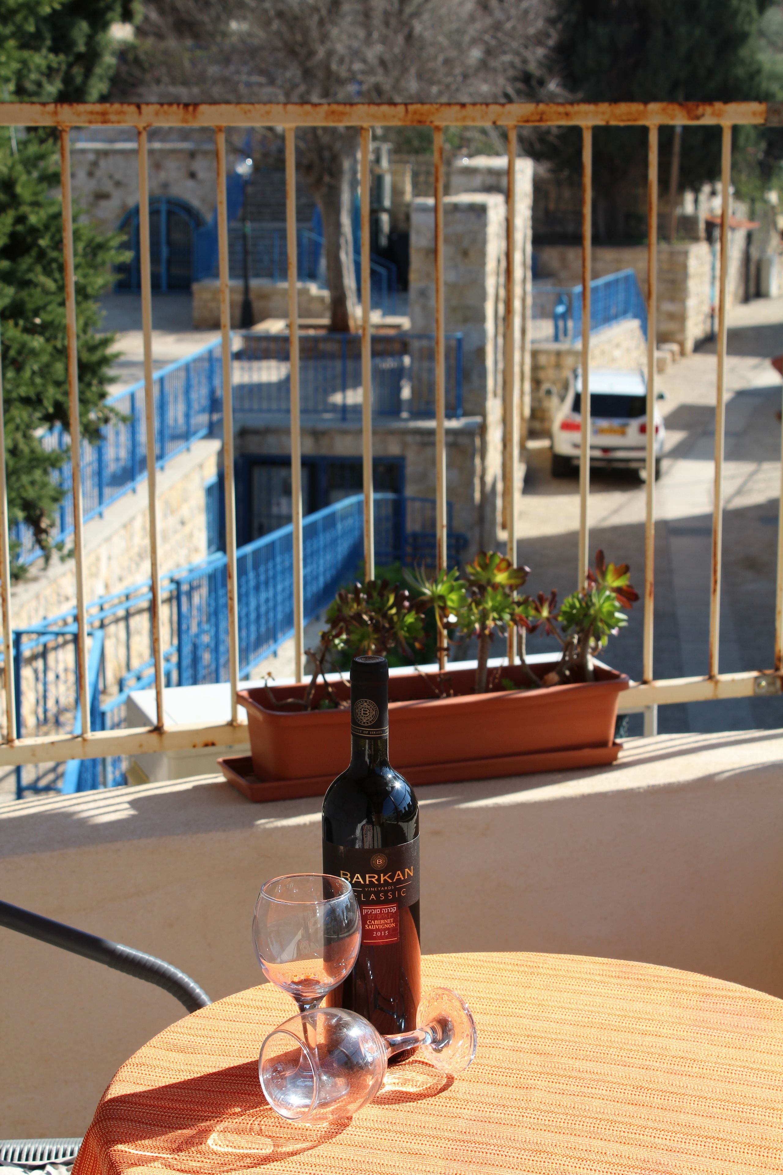 Un balcón con una mesa que sostiene una botella de vino y dos copas.