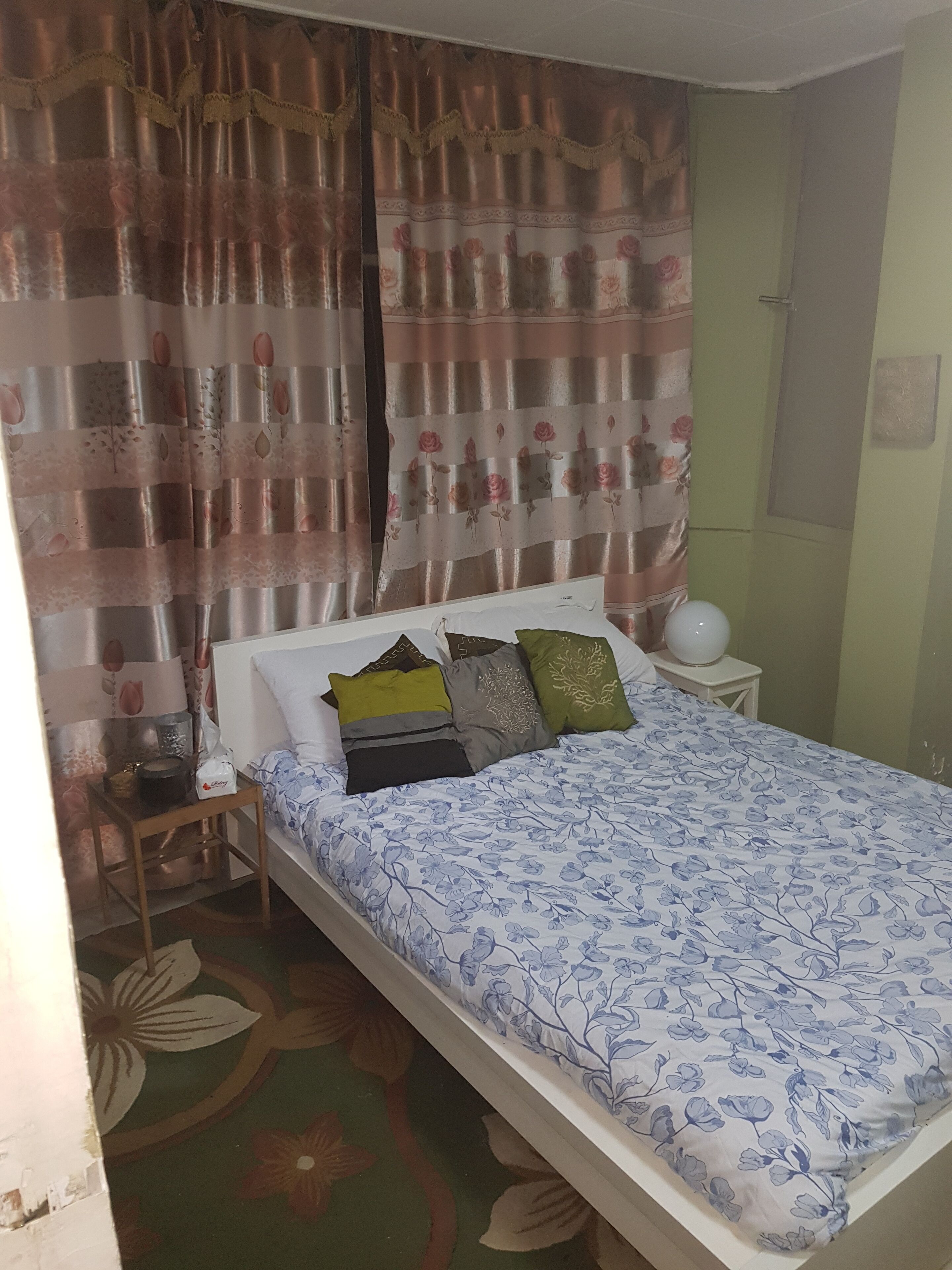 Un dormitorio con cama, almohadas, mesita de noche, lámpara y cortinas.
