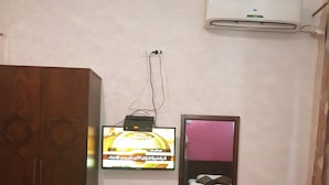 A room with a wooden wardrobe, a television mounted on the wall, a small shelf with a remote control, and an air conditioning unit above the shelf. - Downtown Inn (Cairo)