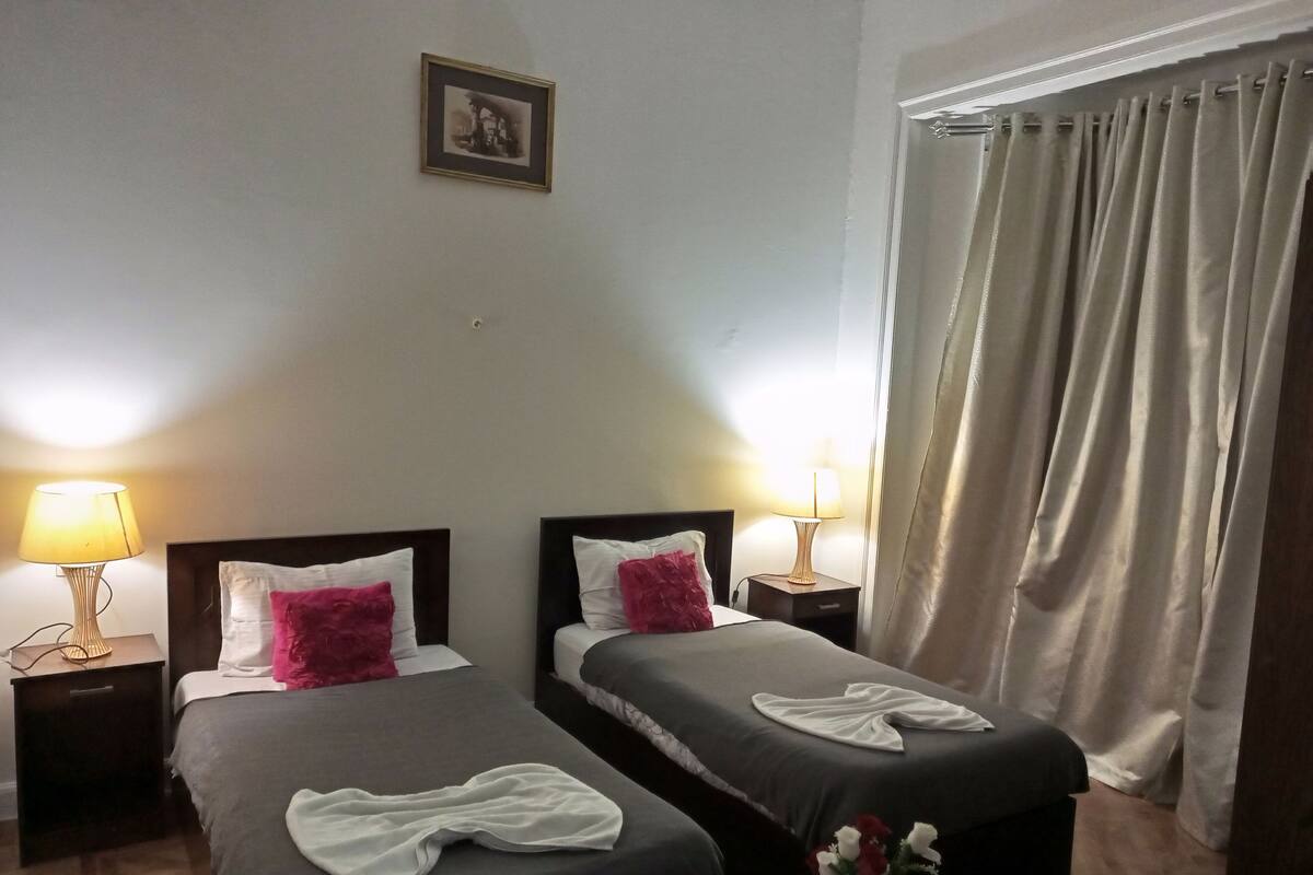 A hotel room with two beds, each with a nightstand, a lamp, and a picture on the wall.