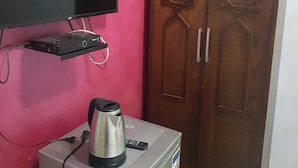 A room with a pink wall, a wooden wardrobe with star-shaped cutouts, a flat-screen TV mounted on the wall, and a small refrigerator with a kettle on top. - Downtown Inn (Cairo)