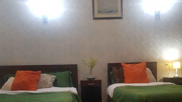 A room with two beds, each with green bedding and orange pillows, a small nightstand with a vase of flowers, and a framed picture on the wall. - Downtown Inn (Cairo)