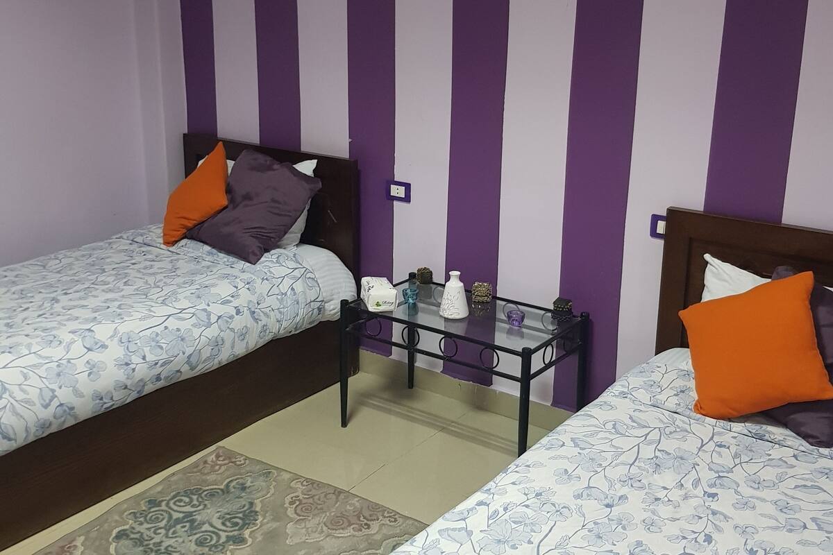 A room with two beds, a small table, and a wall with vertical stripes.