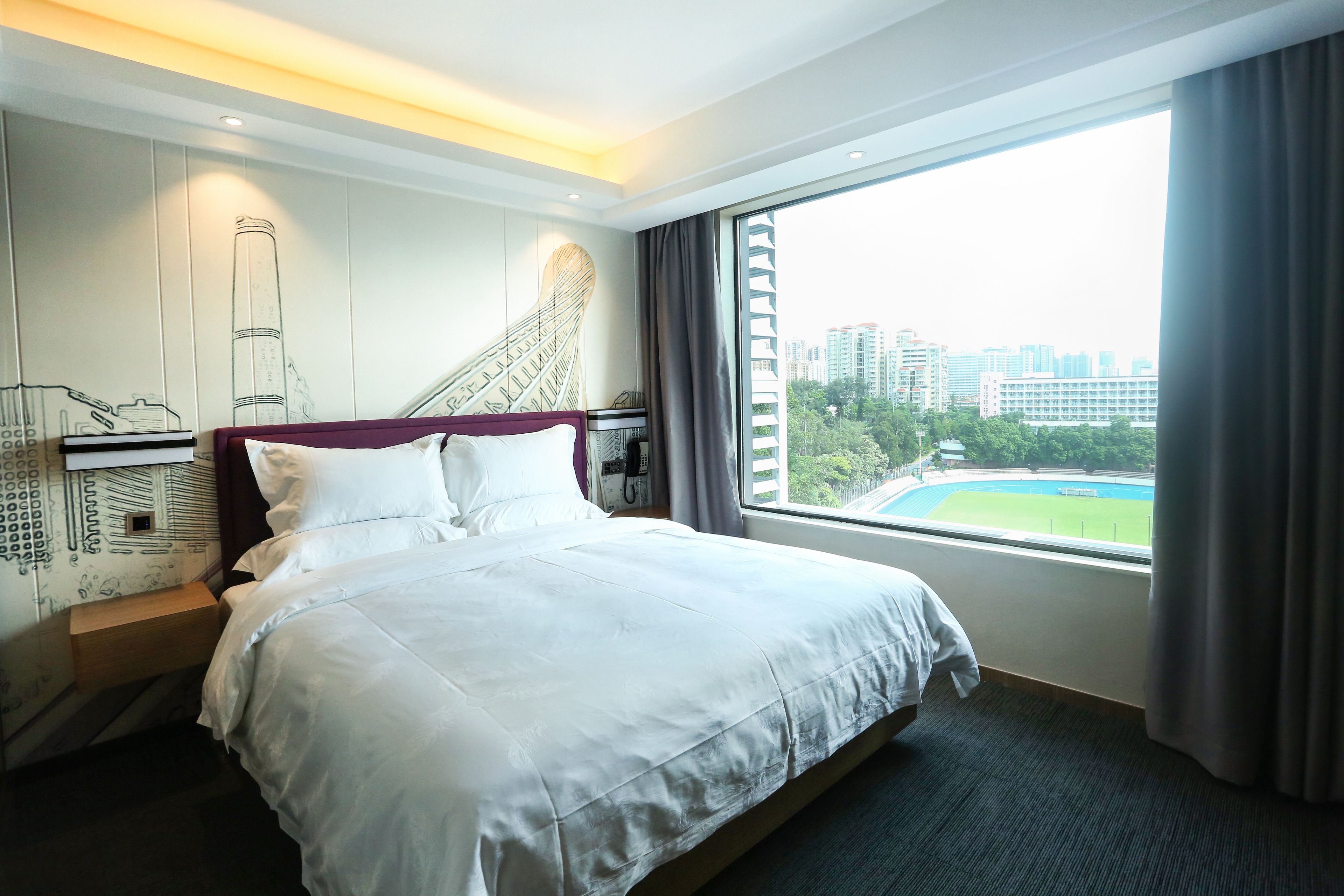 A hotel room with a large bed, a city view, and a mural on the wall.