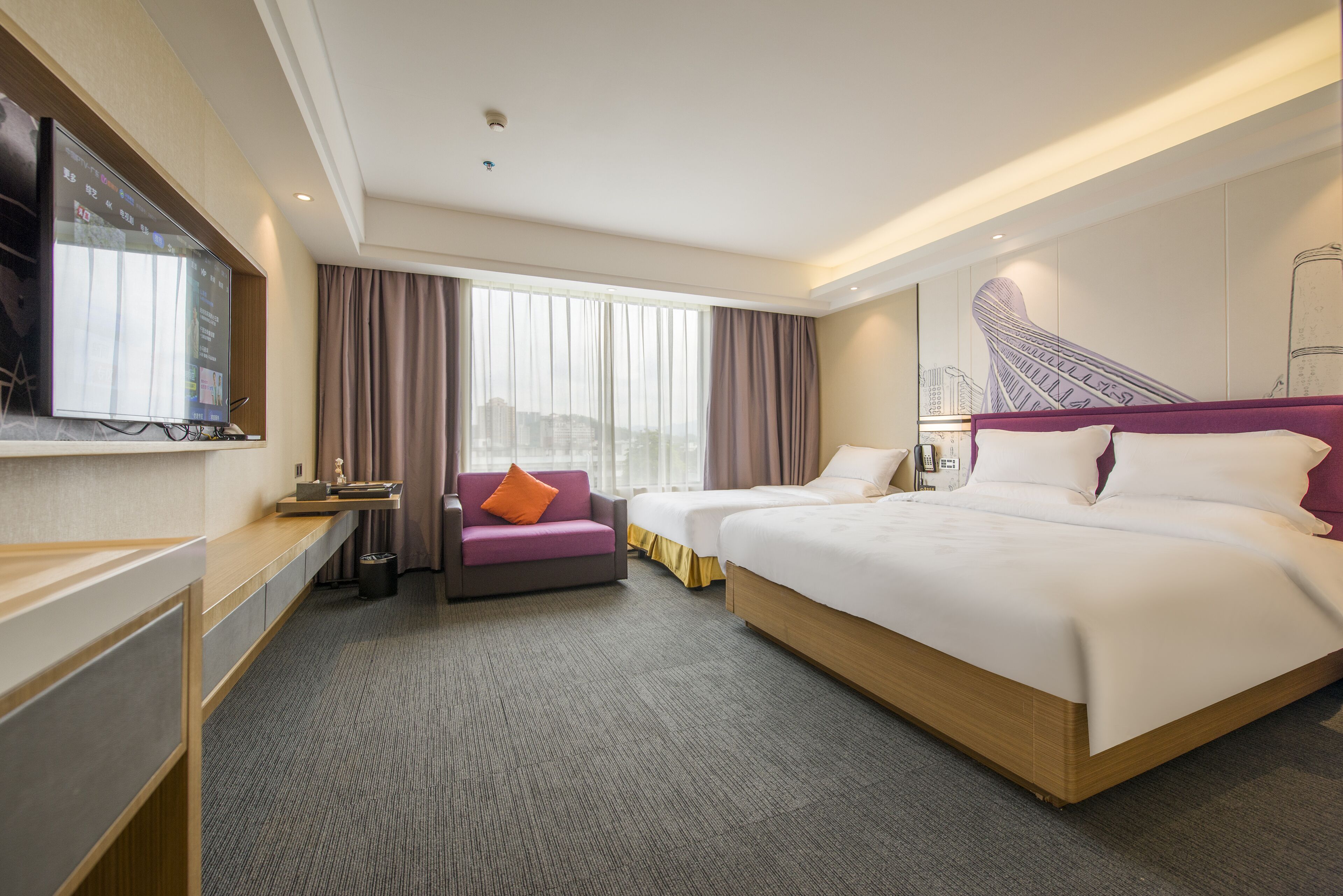 A hotel room with a large bed, a desk with a computer, a chair, and a TV mounted on the wall.