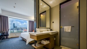A hotel room with a large window, a bed, a wooden vanity with a mirror, and a glass shower door. - Yizhi flat (Guangzhou Zhujiang New Town Huashi Subway Station Branch) (Guangzhou)