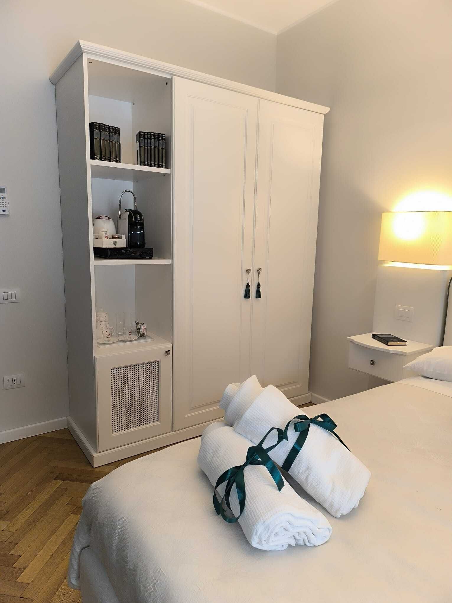 A hotel room with a large wardrobe, a bedside table with a lamp, and neatly folded towels on the bed.