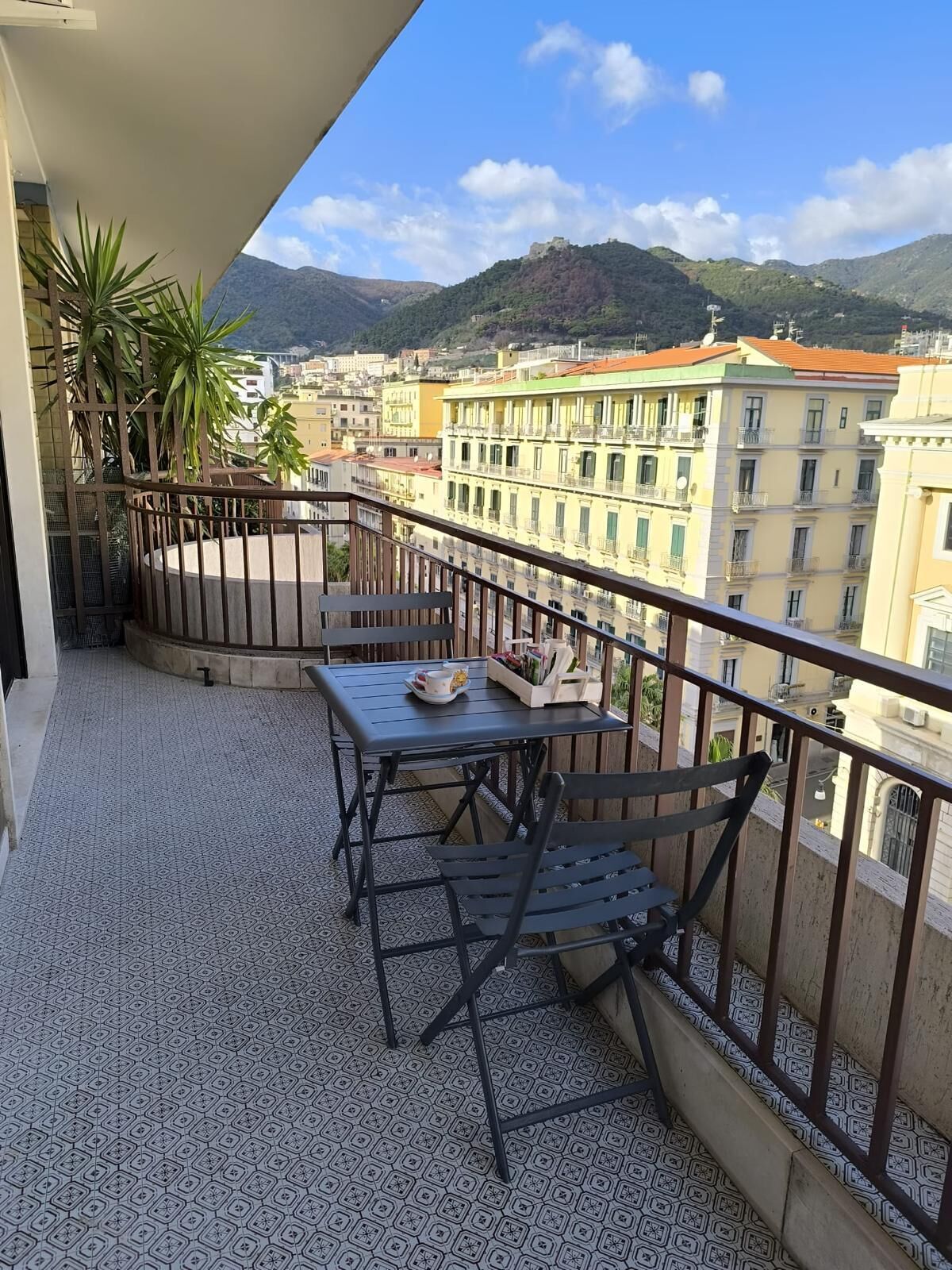 Een balkon met een tafel en stoelen, met uitzicht op een stadsbeeld met gebouwen en bergen.