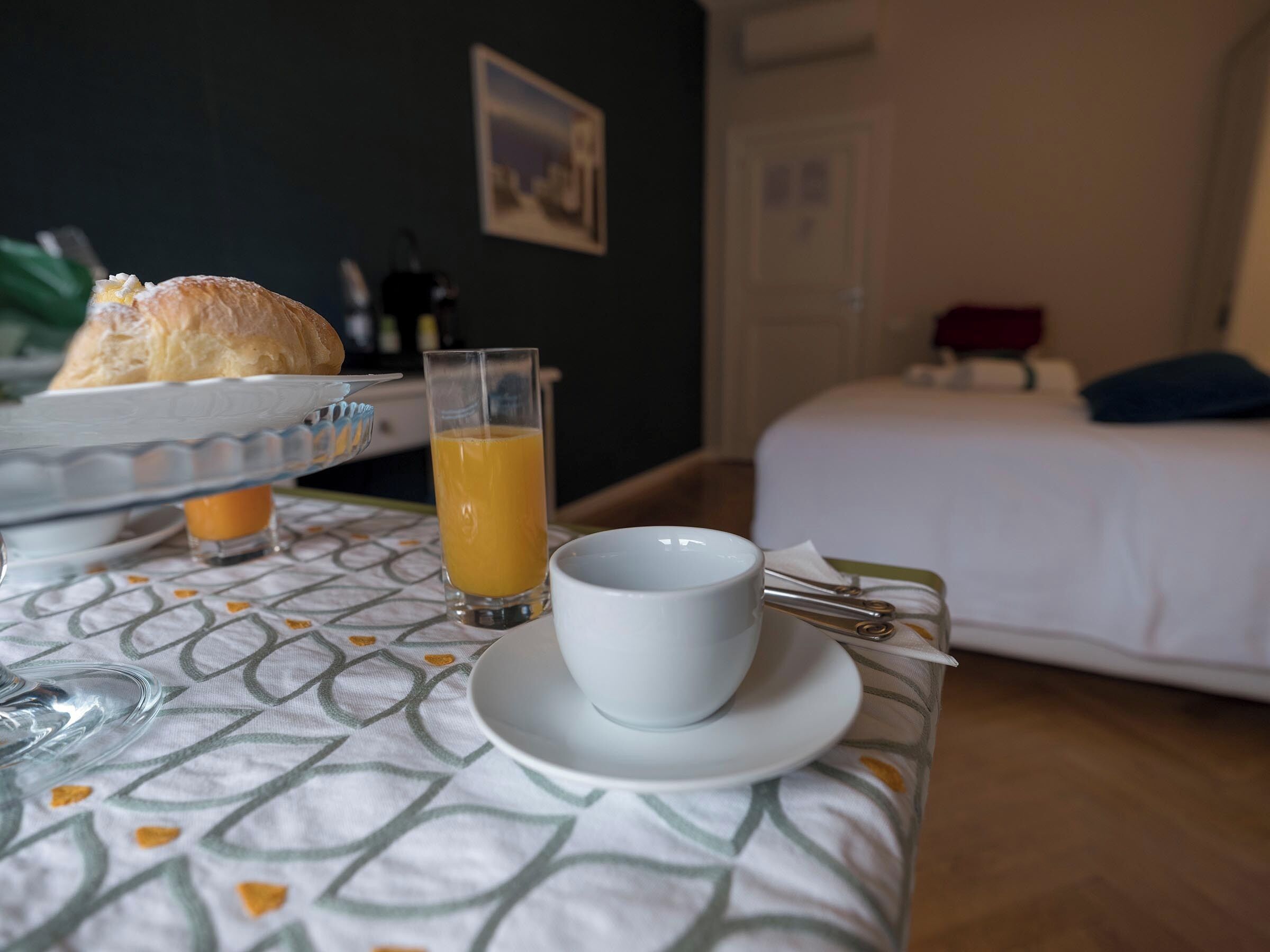 A breakfast setup with bread, orange juice, and a cup on a patterned tablecloth.