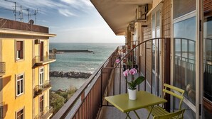 Uma varanda com uma mesa e cadeiras amarelas, com vista para a costa, edifícios e o mar.