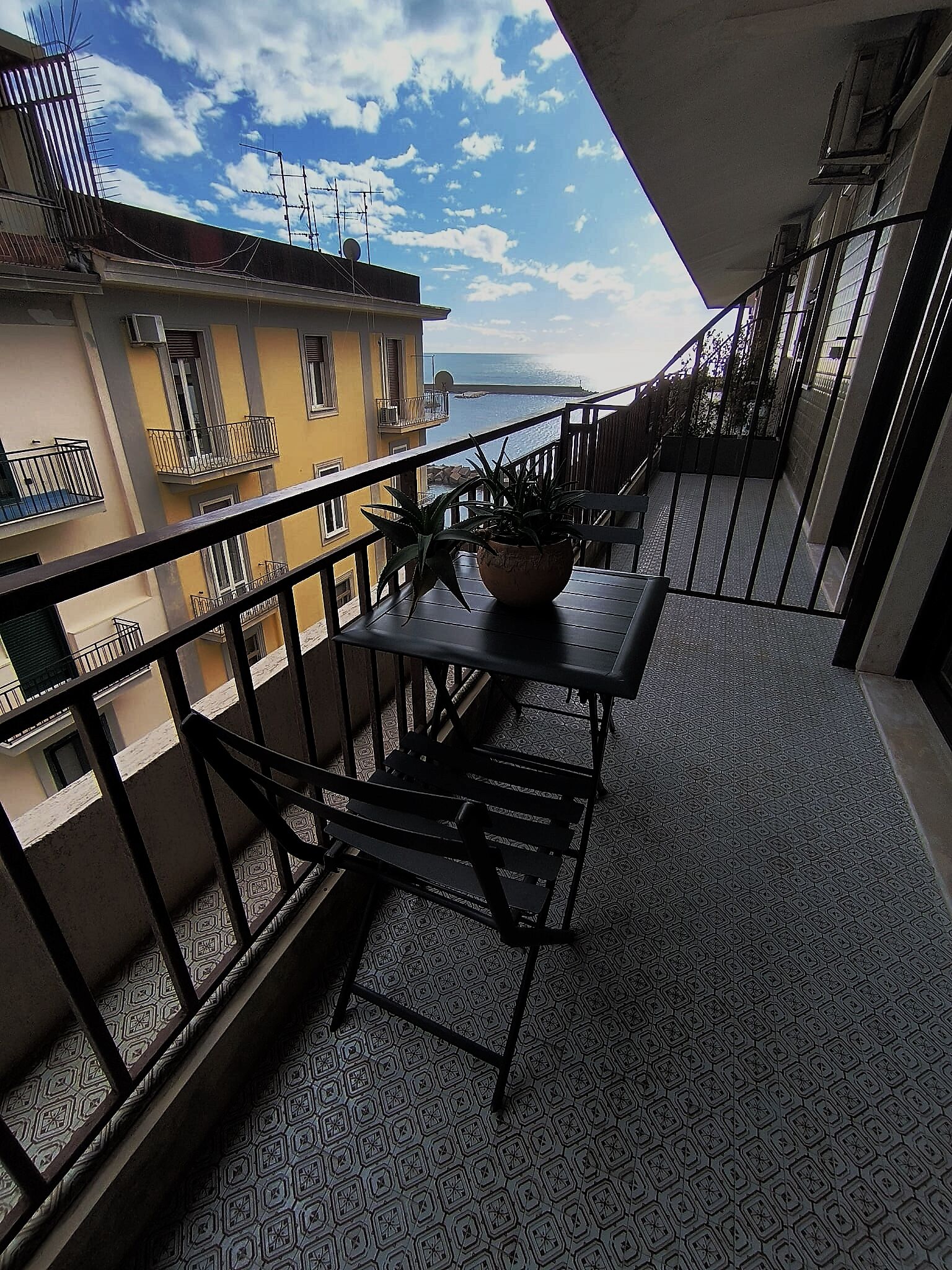 A balcony with a view of the sea, a potted plant, and a table.
