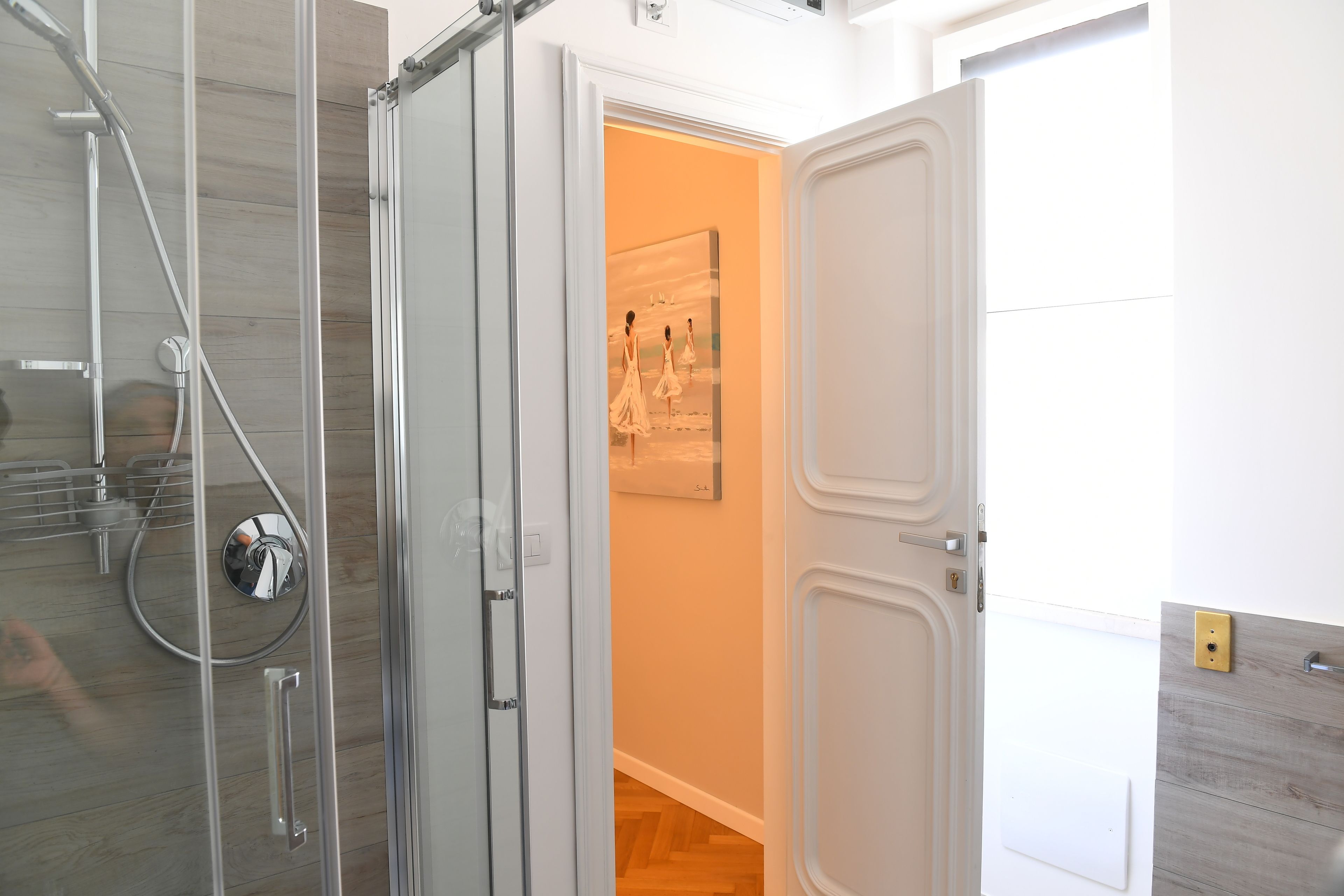 A modern bathroom with a glass shower enclosure, a white door, and a wooden floor.
