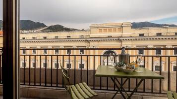A balcony with a table set for two, a chair, and a view of a historic building with columns and a mountain in the background.