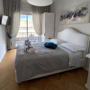 A hotel room with a bed, a wardrobe, a TV, and a balcony with curtains. - Attico 195 (Salerno)