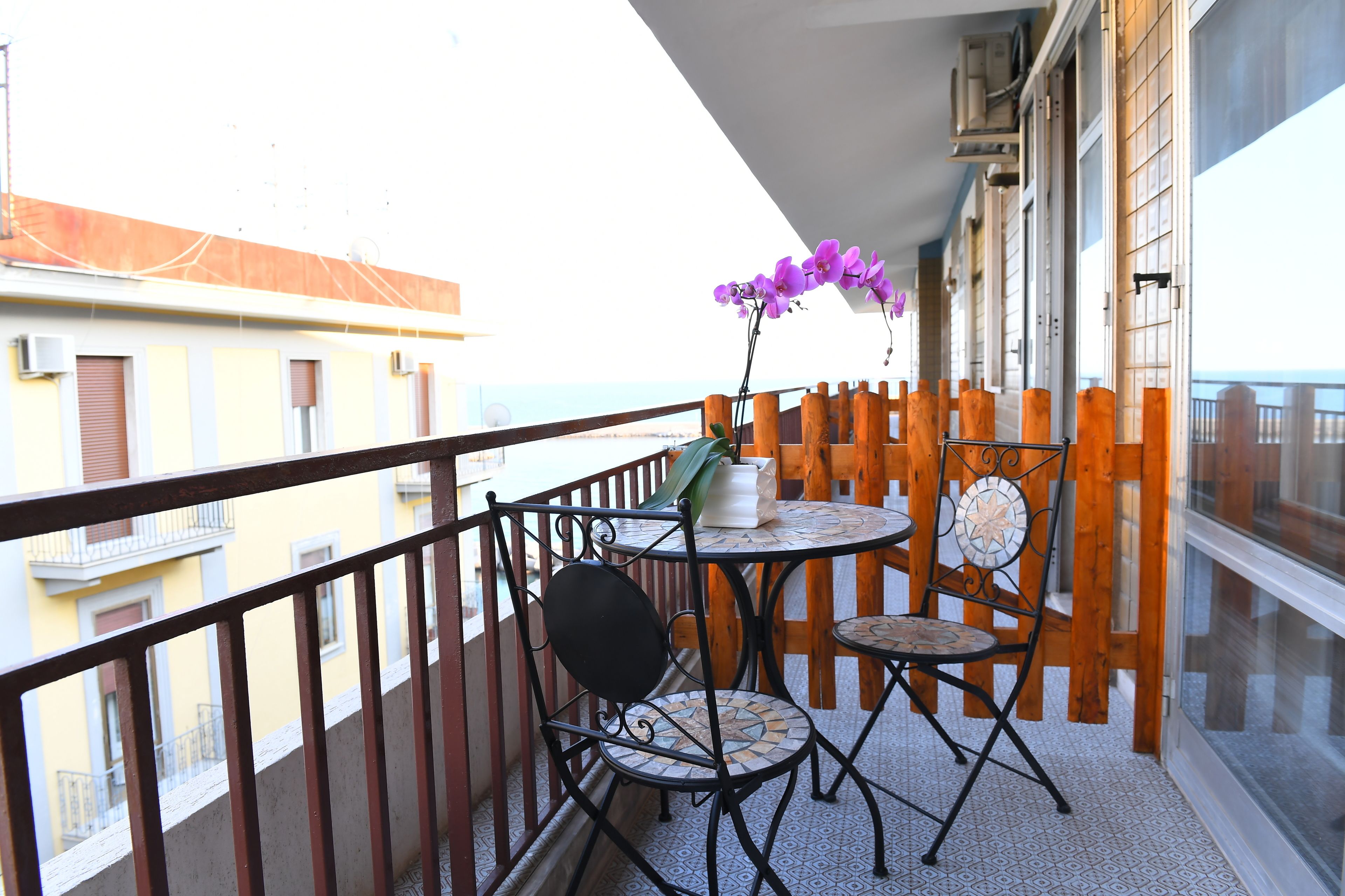 Ein Balkon mit Tisch und Stühlen, einem Blumentopf und Blick auf die Stadtlandschaft.