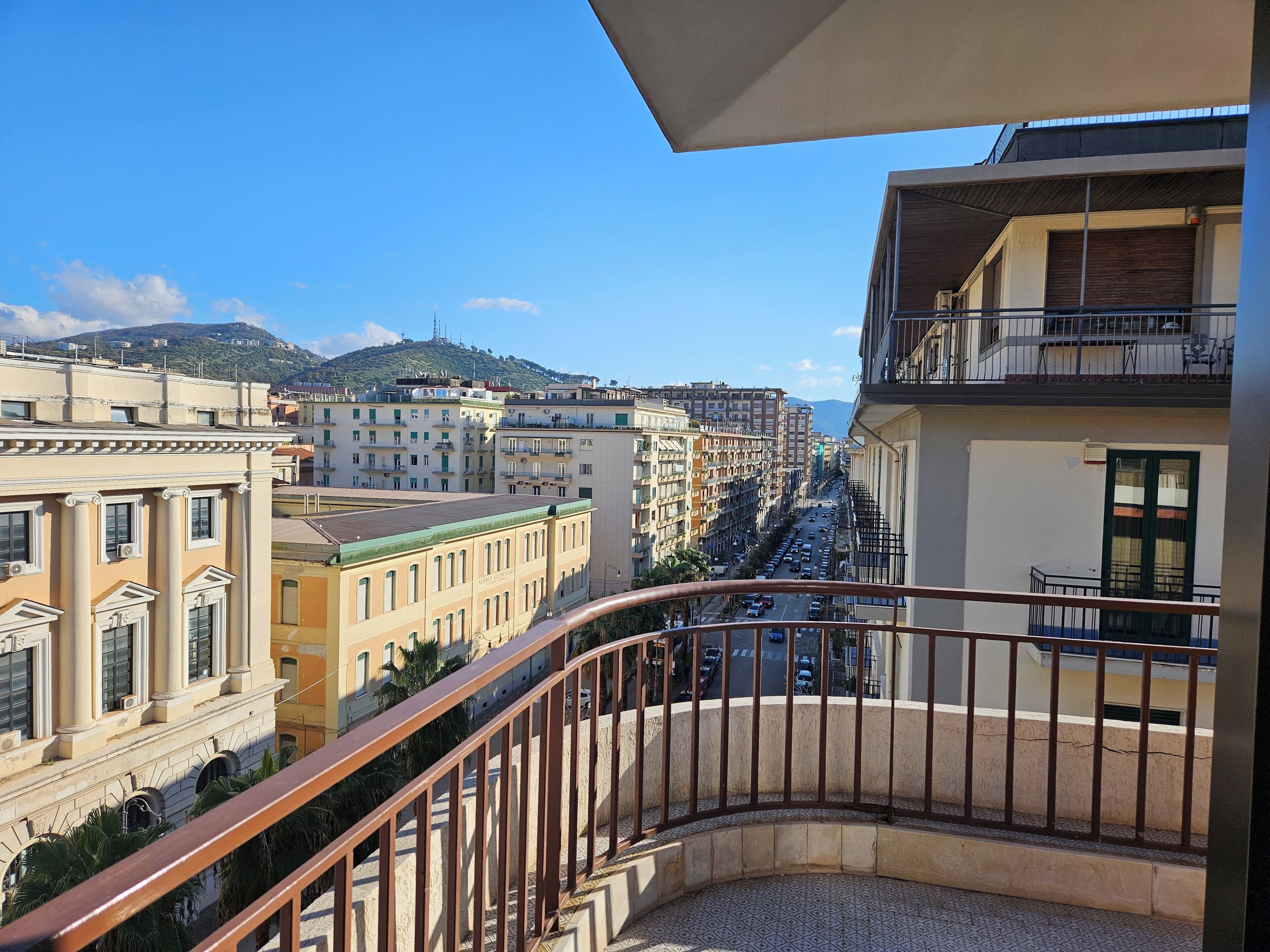 A balcony with a view of a city street, buildings, and a distant mountain.