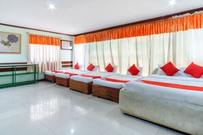A hotel room with four beds, each with red pillows, white bedding, and orange curtains. There is a green metal shelf and a framed picture on the wall. - Maanyag Pension House (Mandaue)