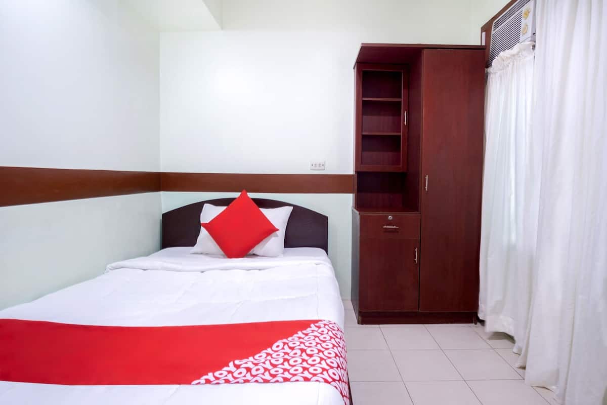 Un lit bien fait, avec un oreiller rouge, une armoire en bois et un rideau blanc.