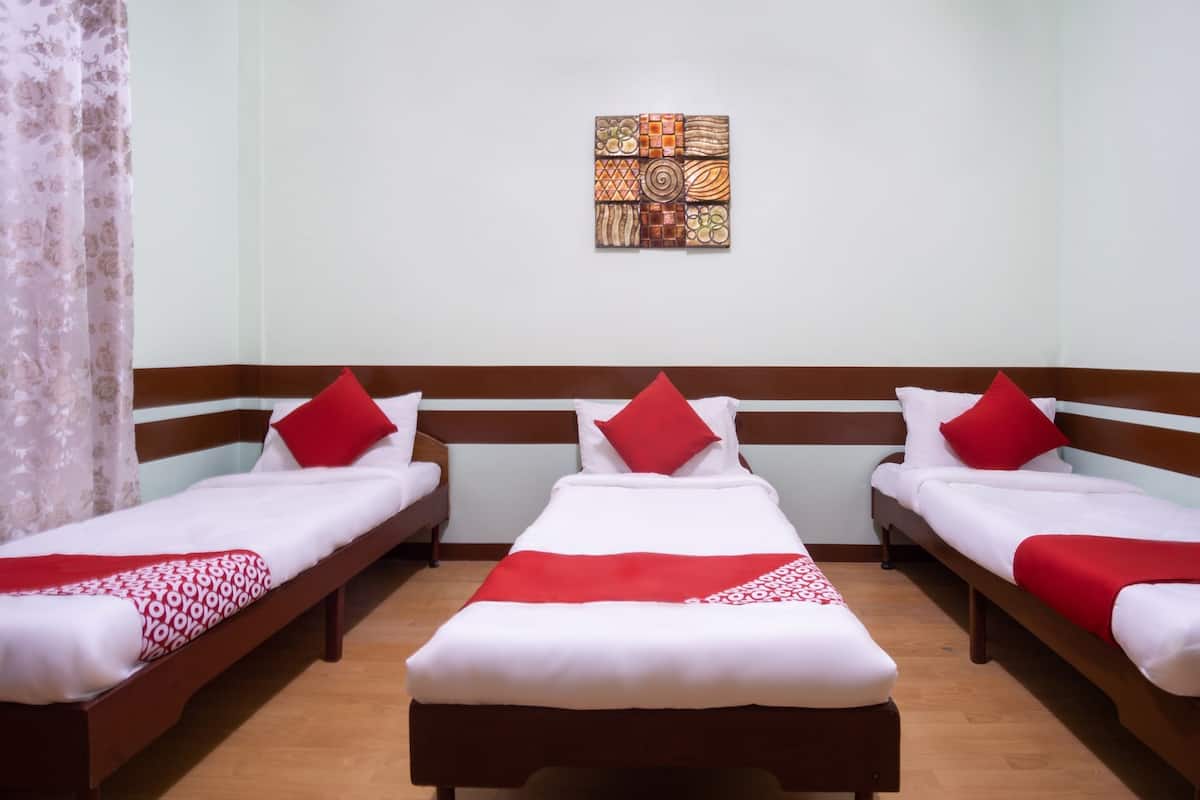 Une chambre d’hôtel avec trois lits simples, chacun recouvert d’une courtepointe rouge et blanche assortie à des oreillers du même style. Une œuvre d’art décorative est accrochée au mur, au centre, au-dessus des lits.
